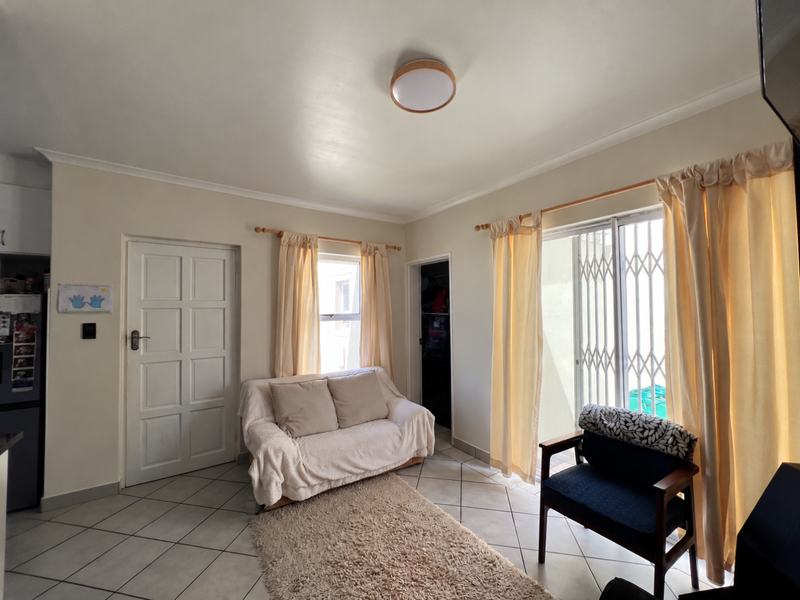 A living room featuring ceramic floor tiles, a sliding glass door with security gate, and a panel door leading to adjacent spaces.