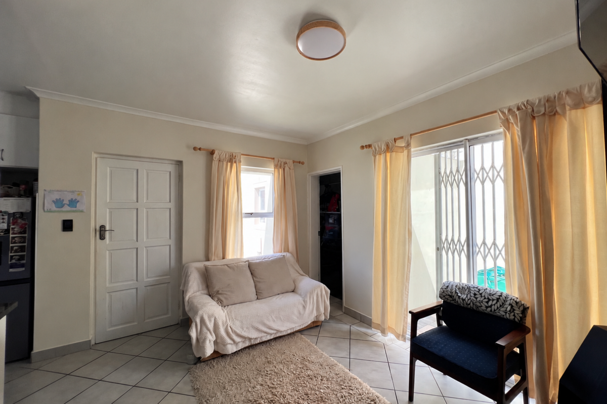 A living room featuring ceramic floor tiles, a sliding glass door with security gate, and a panel door leading to adjacent spaces.