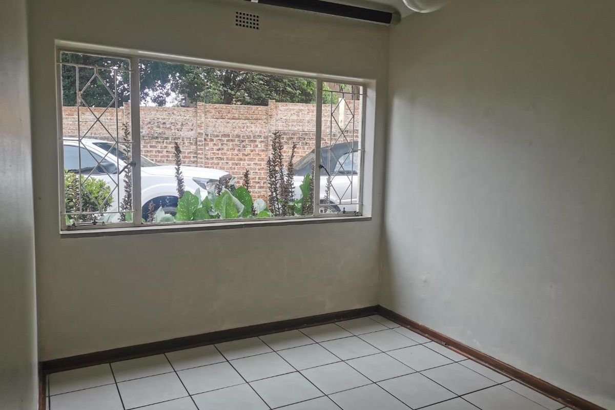 An empty living room featuring tiled flooring, a large window with security bars, and neutral wall finishes, offering a blank canvas for personalization.