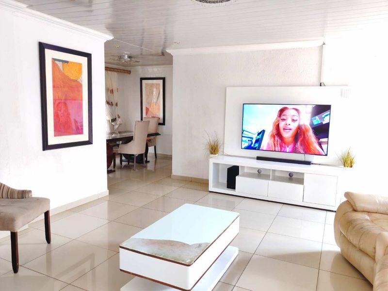 Open-plan living area featuring tiled flooring, a tongue and groove ceiling, and a built-in media wall unit, creating a bright and functional space.