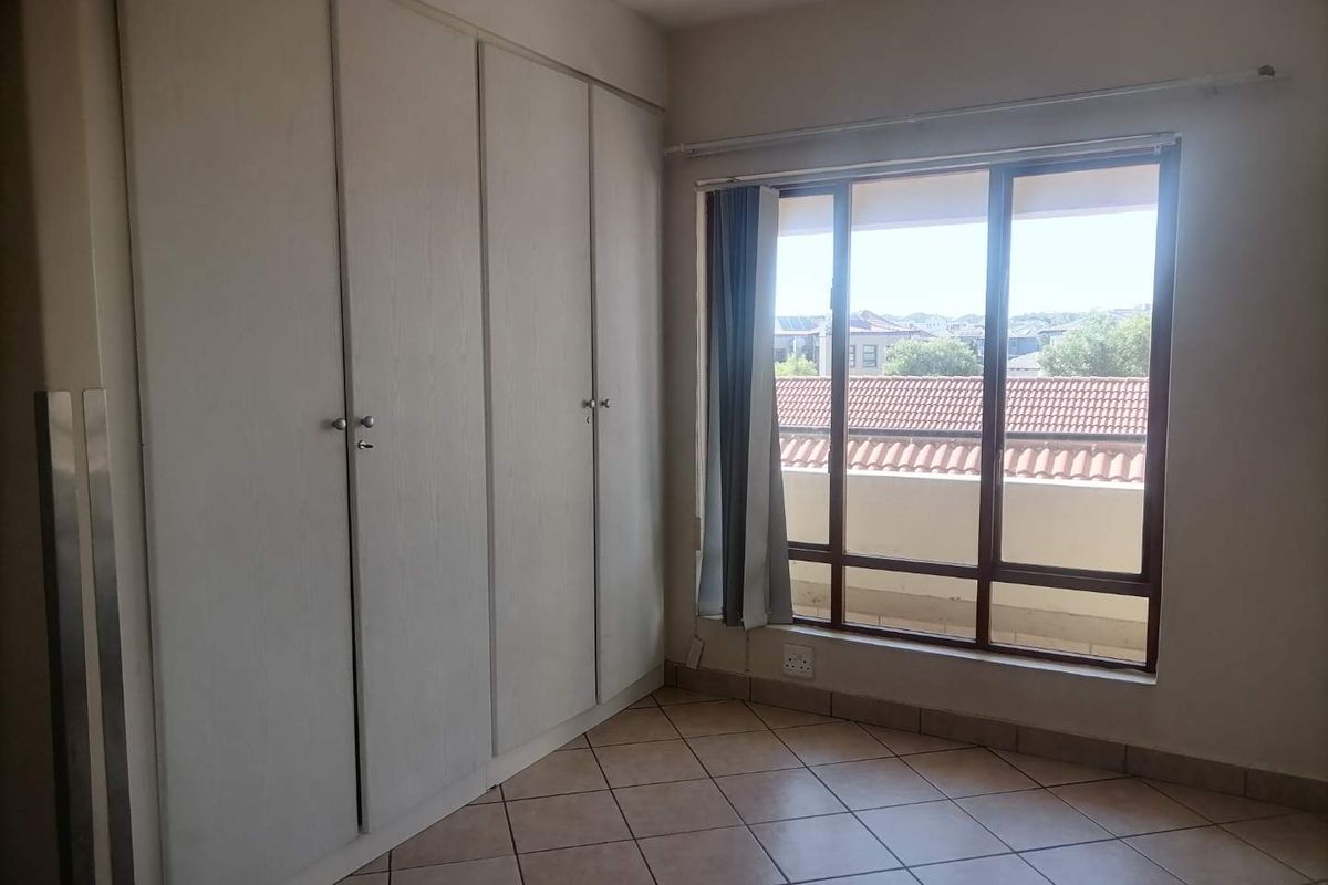A bedroom featuring built-in cupboards, tiled flooring, and a large window providing natural light and an exterior view.