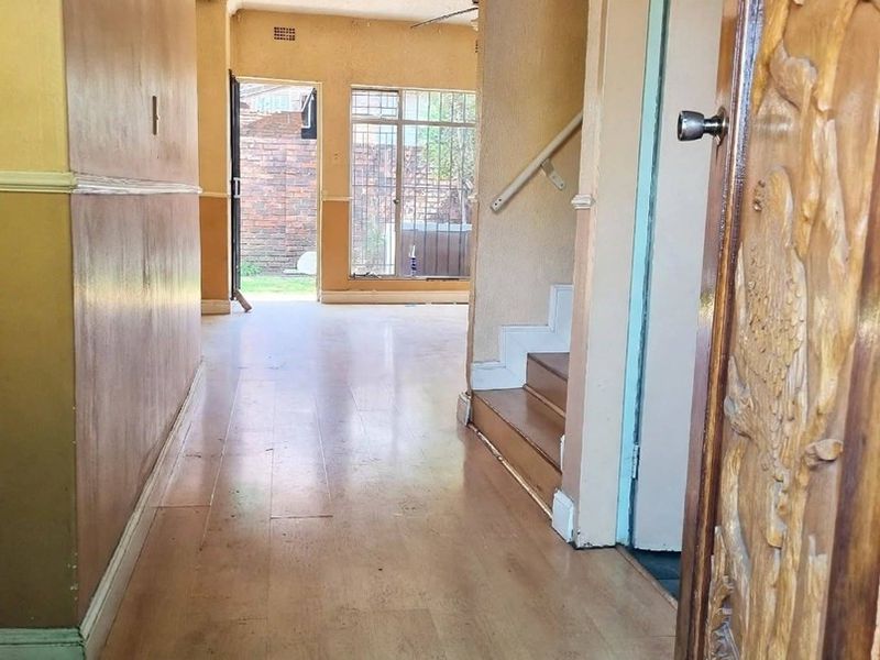 A vacant hallway featuring laminate flooring and a staircase with a handrail, leading towards an open living area with access to the rear exterior.