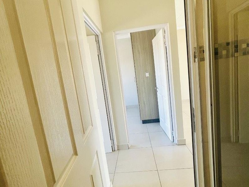 A bright hallway featuring tiled flooring and access to multiple rooms, including a space with built-in cupboards and a shower enclosure.