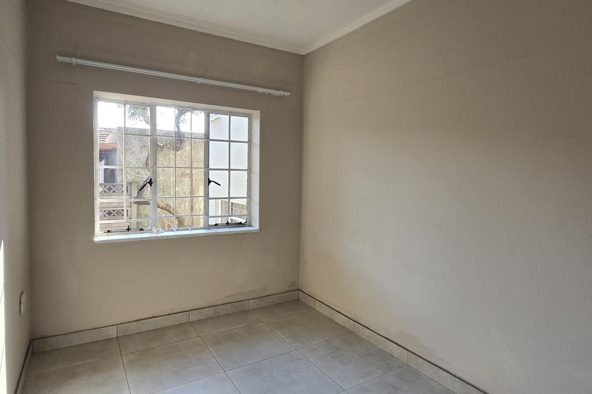 An empty bedroom featuring tiled flooring, neutral walls, and a window with security bars, offering a blank canvas for personalization.