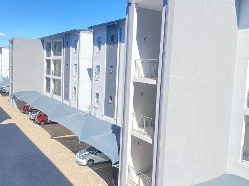 Exterior view of a modern apartment complex featuring multi-level units with balconies and covered parking bays.