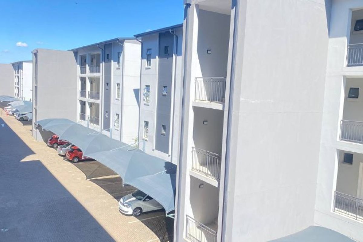Exterior view of a modern apartment complex featuring multi-level units with balconies and covered parking bays.
