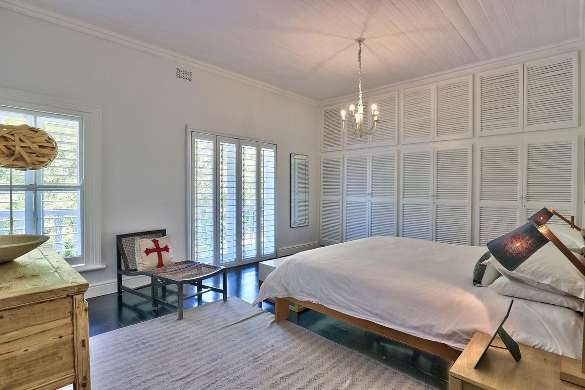 Spacious bedroom featuring timber flooring, extensive built-in wardrobe storage, and classic shutter blinds, creating a bright and well-maintained living space.