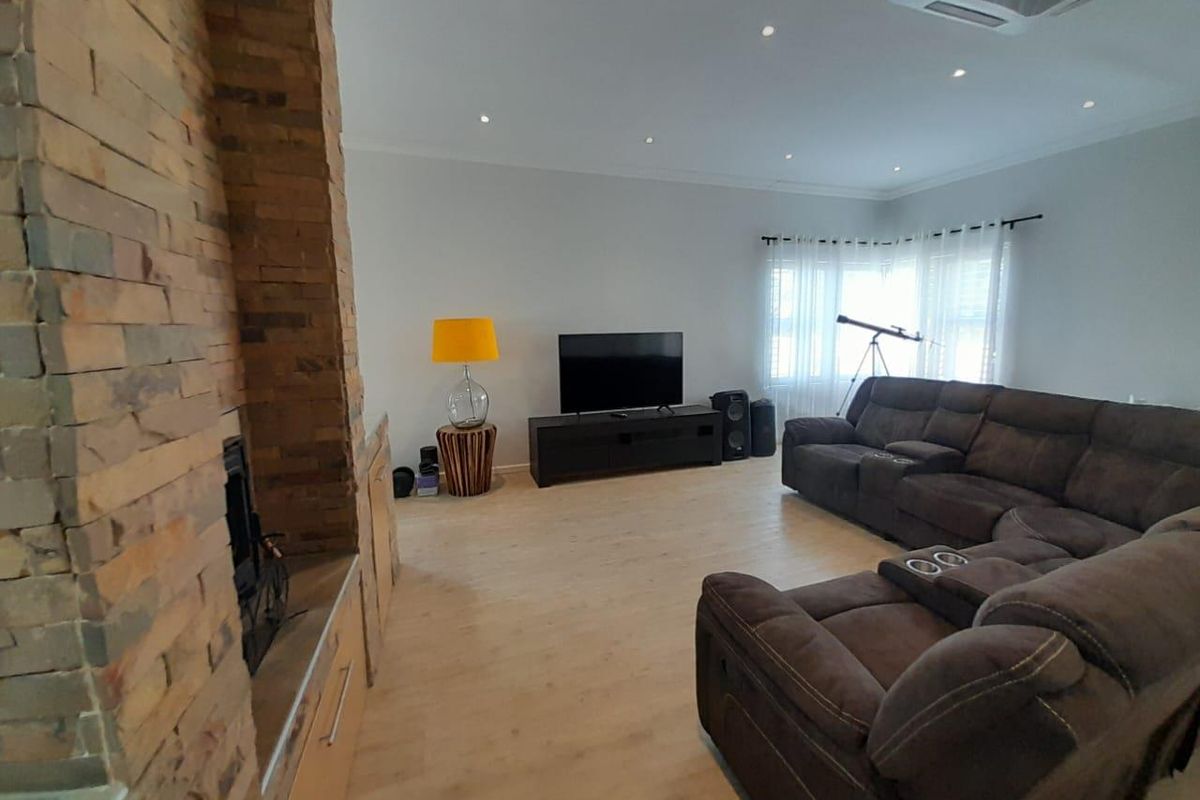Spacious living room featuring a prominent stone-clad fireplace, recessed downlighting, and light-toned wood-look flooring.