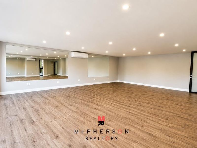 A spacious, well-lit room featuring laminate flooring, recessed downlighting, wall-mounted mirrors, and a split-system air conditioner, suitable for a home gym or studio.