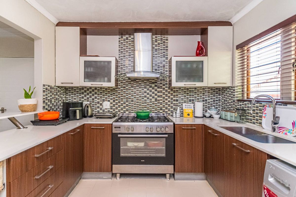 A functional U-shaped kitchen featuring wood-finish cabinetry, stone countertops, a mosaic tile backsplash, and a stainless steel gas stove with an extractor fan.