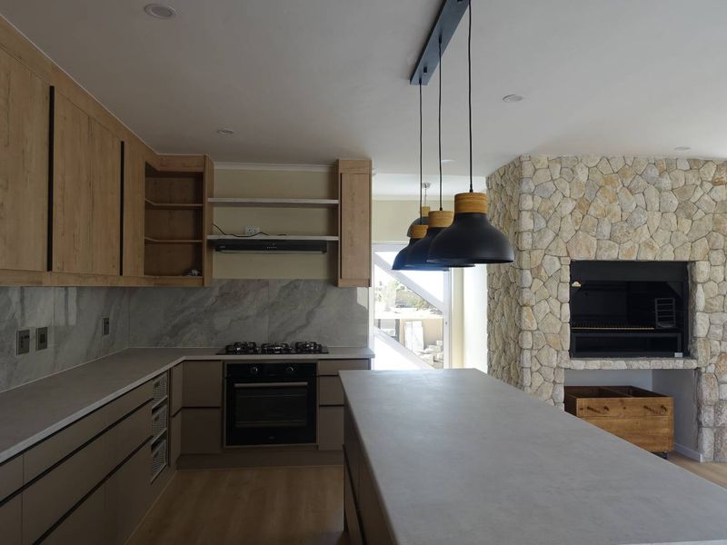 Modern open-plan kitchen featuring a large island, stone countertops, built-in oven, gas hob, and a striking stone-clad indoor fireplace.