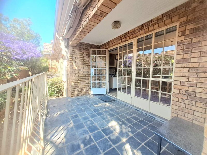 A covered patio area featuring brick walls, tiled flooring, and classic french doors leading into the home, complemented by a metal balustrade.