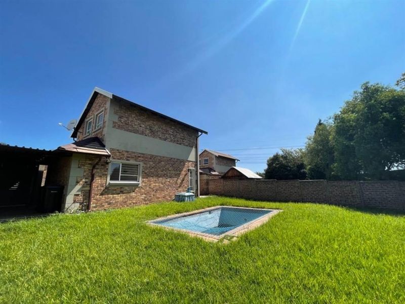 Rear exterior view of the property featuring a private swimming pool with a safety net, set within a spacious garden with brick boundary walls.
