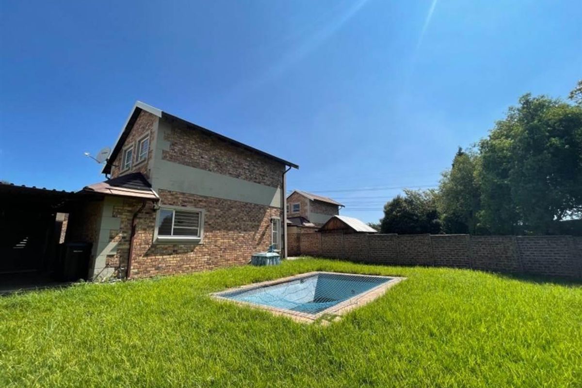 Rear exterior view of the property featuring a private swimming pool with a safety net, set within a spacious garden with brick boundary walls.