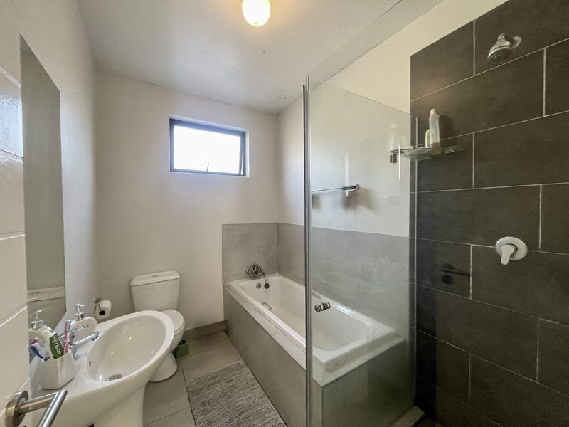 A functional bathroom featuring a pedestal basin, toilet, and a combined bathtub with a glass shower screen and dark tiled surround.