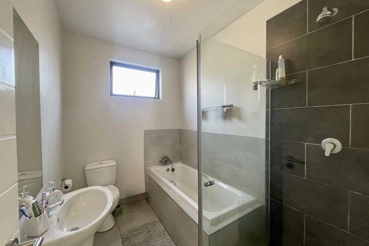 A functional bathroom featuring a pedestal basin, toilet, and a combined bathtub with a glass shower screen and dark tiled surround.