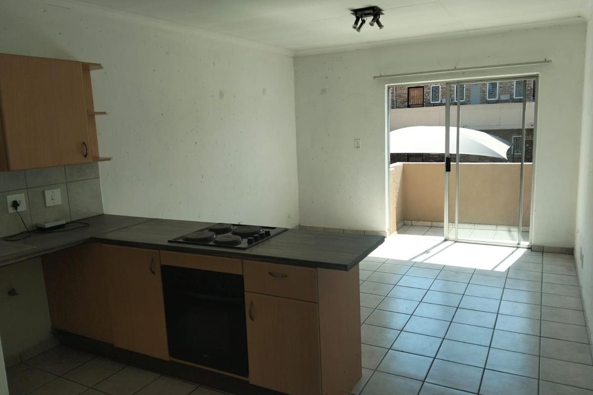 Open-plan kitchen and living area featuring tiled floors, built-in cabinetry with integrated oven and hob, and direct access to a private balcony.
