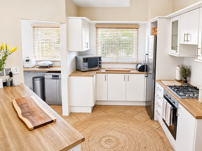 A bright, well-maintained kitchen featuring white cabinetry, wooden countertops, a gas hob, and an adjoining scullery area with natural light.