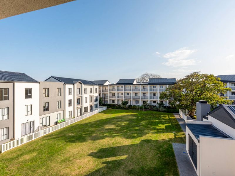 An elevated view of a well-maintained communal garden area surrounded by modern apartment blocks with metal roofing and balcony access.