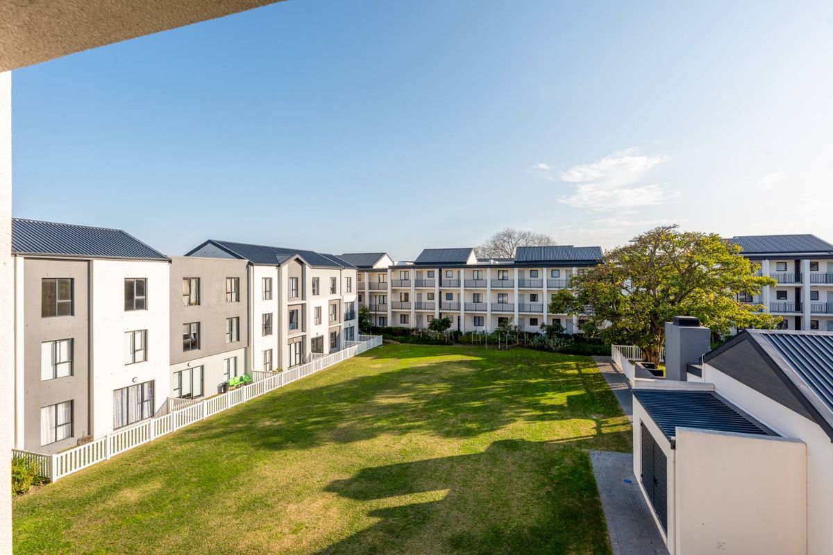 An elevated view of a well-maintained communal garden area surrounded by modern apartment blocks with metal roofing and balcony access.