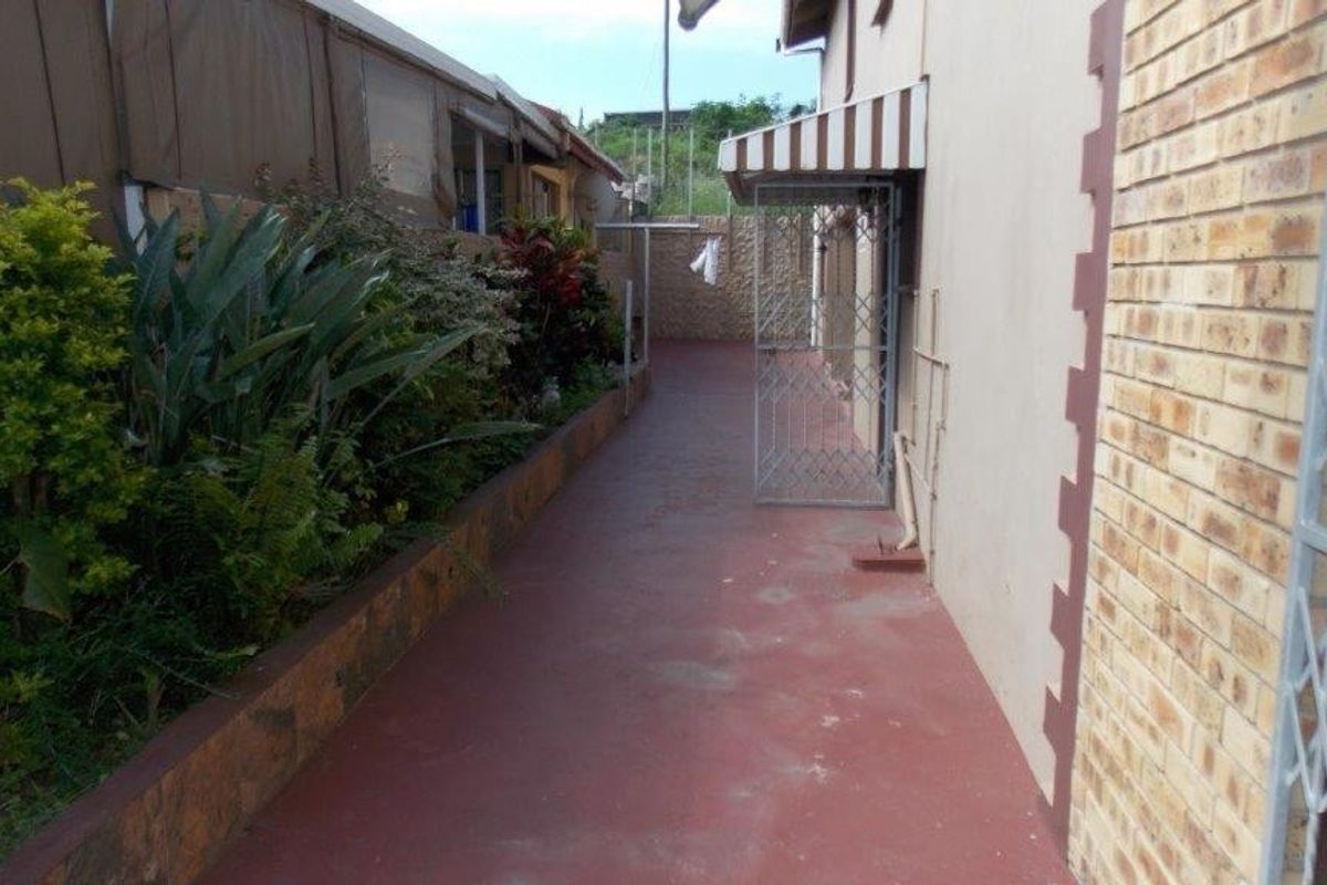 A side exterior walkway featuring a paved path, raised garden beds, and security gates along the brick building facade.