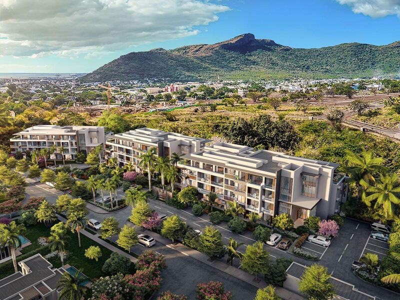 An aerial view of a modern residential development featuring multi-story apartment buildings, landscaped grounds, and parking areas set against a scenic mountain backdrop.