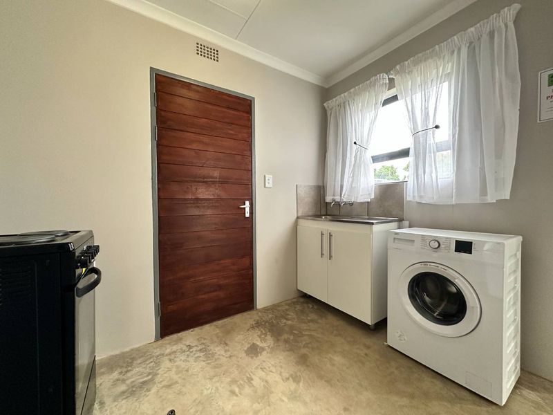 Functional laundry room featuring a stainless steel sink, built-in cabinetry, tiled splashback, and direct access via a solid timber door.