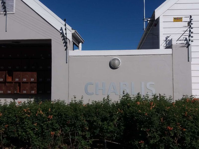 Front entrance area of Chablis apartment complex featuring a wall-mounted post box bank, electric security fencing, and exterior lighting.