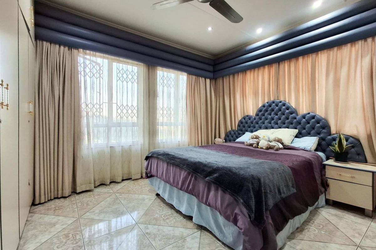 Spacious bedroom featuring tiled flooring, built-in cupboards, and a ceiling fan, with large windows fitted with security gates.