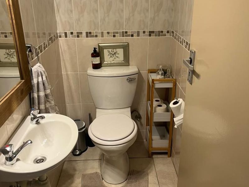 A compact guest bathroom featuring neutral ceramic wall and floor tiles, a pedestal basin, and a standard close-coupled toilet.