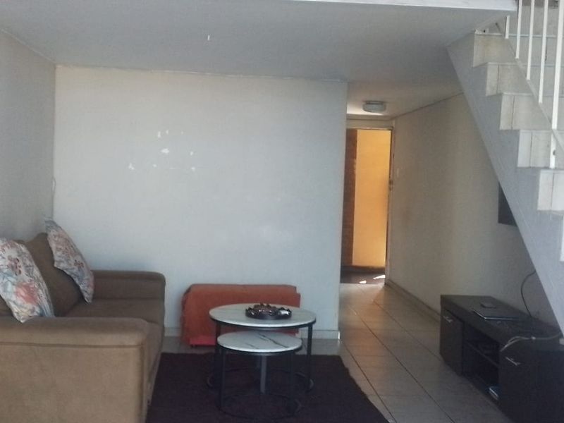 A living room area featuring tiled flooring and a staircase with a metal railing, showing signs of wear on the walls.