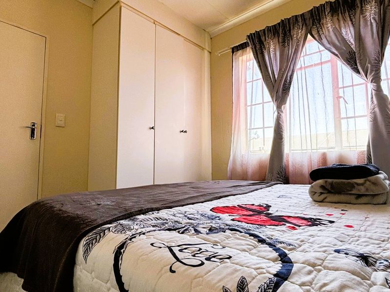 A bedroom featuring a built-in wardrobe and a window with security bars, providing natural light and functional storage space.