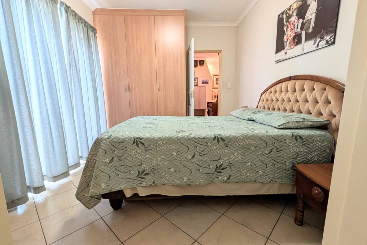 A functional bedroom featuring built-in wooden cupboards, tiled flooring, and large windows with curtains, offering a comfortable and practical living space.