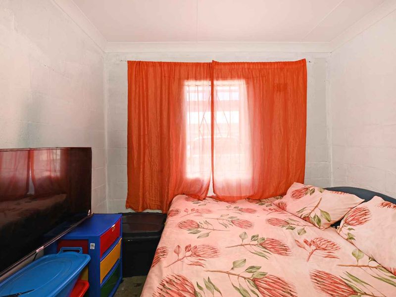 A bedroom featuring exposed concrete block walls and a window fitted with security bars.