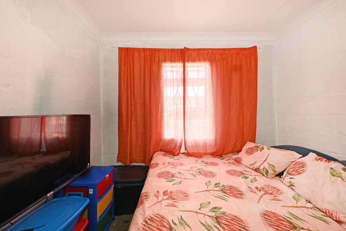 A bedroom featuring exposed concrete block walls and a window fitted with security bars.