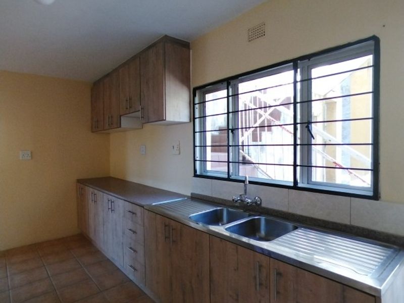 A functional kitchen featuring wood-look built-in cabinetry, a double stainless steel sink, tiled flooring, and a window with security bars.