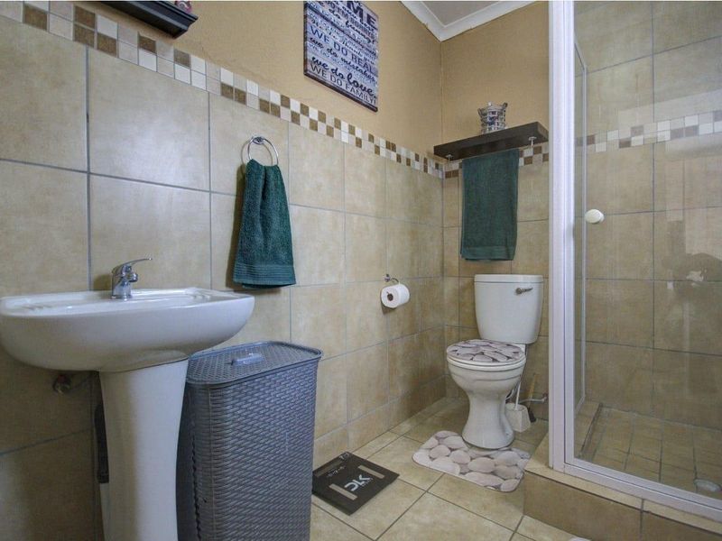 A functional bathroom featuring a pedestal basin, toilet, and a glass-enclosed shower with neutral ceramic wall and floor tiling.