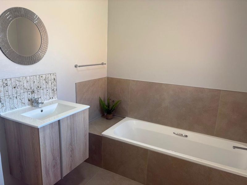A modern bathroom featuring a wood-finish vanity with a basin, a built-in bathtub with tiled surround, and a decorative mosaic splashback.