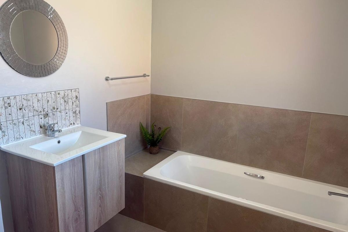 A modern bathroom featuring a wood-finish vanity with a basin, a built-in bathtub with tiled surround, and a decorative mosaic splashback.