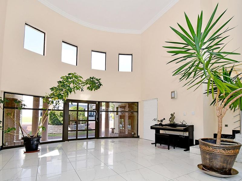 Spacious double-volume entrance hall featuring high ceilings, large glass-panelled doors, and polished tiled flooring with a modern staircase.