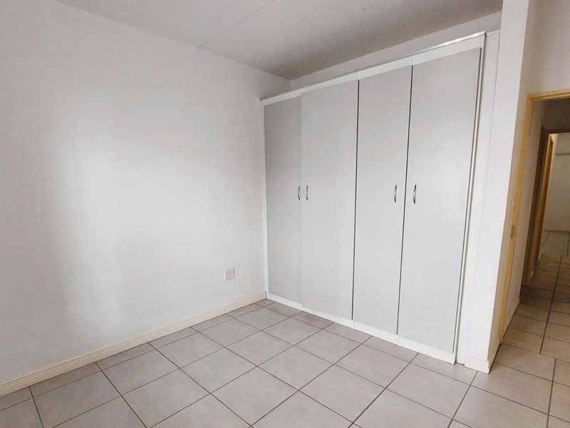 A clean, empty bedroom featuring neutral tiled flooring and built-in cupboards, offering a blank canvas for personalization.
