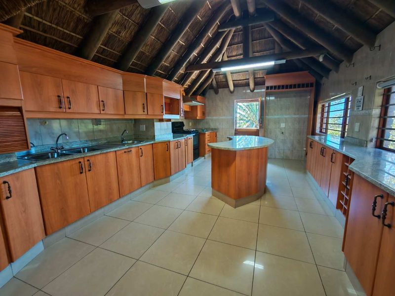 Spacious kitchen featuring a unique thatched roof with exposed timber beams, granite countertops, a central island, and ample wooden cabinetry.