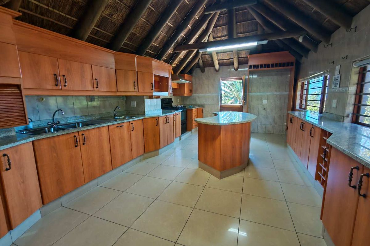 Spacious kitchen featuring a unique thatched roof with exposed timber beams, granite countertops, a central island, and ample wooden cabinetry.