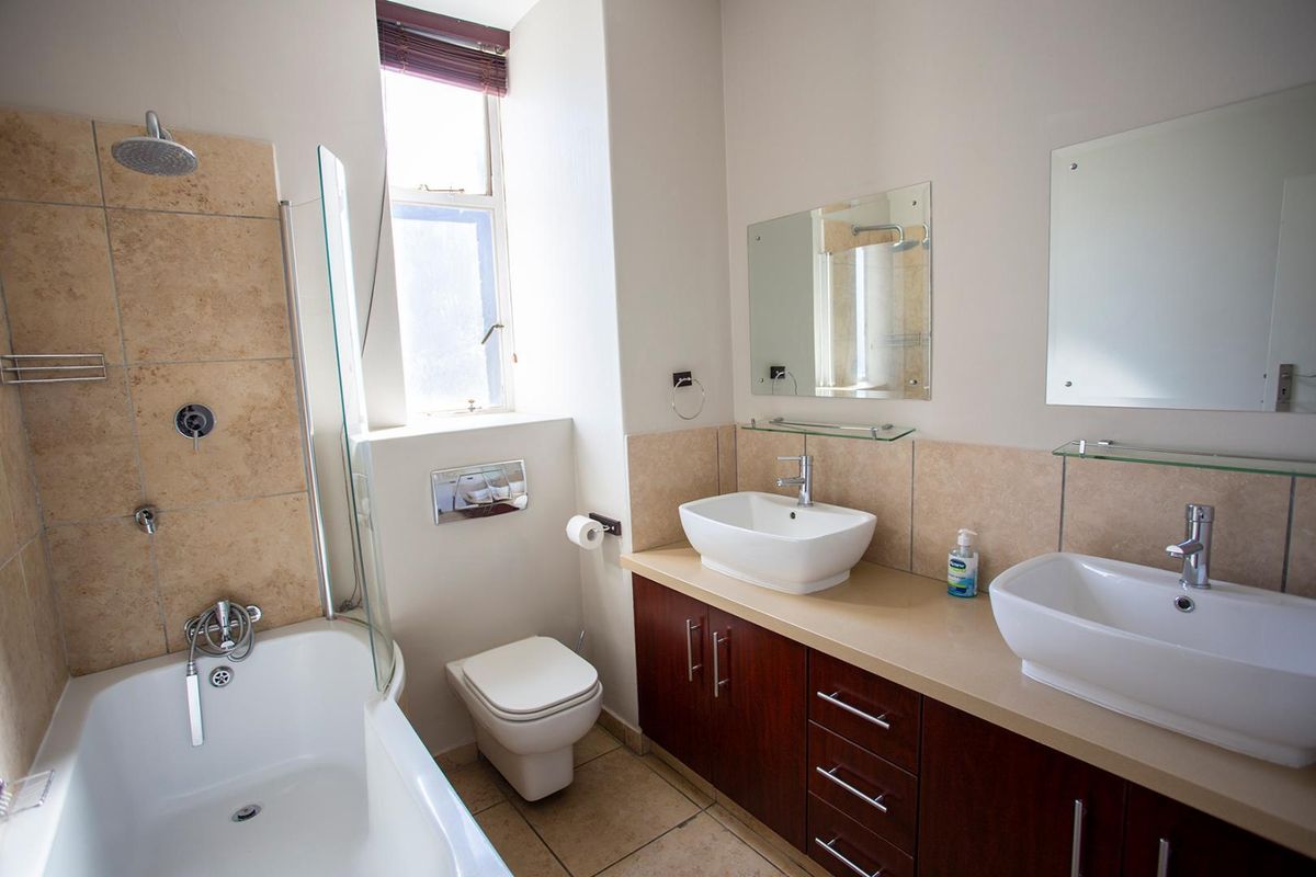 A modern bathroom featuring a double vanity with vessel sinks, a bathtub with an integrated shower, and a wall-mounted toilet.