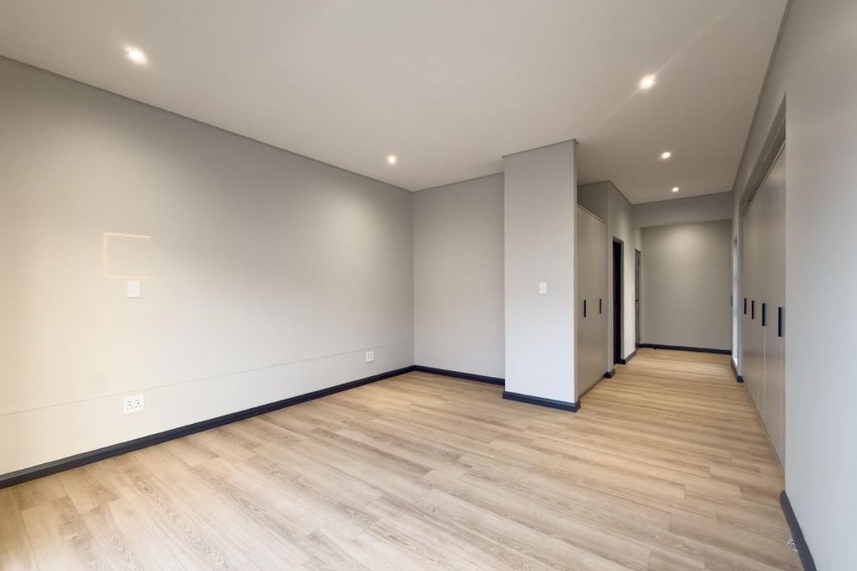 A bright, modern bedroom featuring light wood-look flooring, recessed ceiling lighting, and built-in cabinetry with a clean, neutral finish.