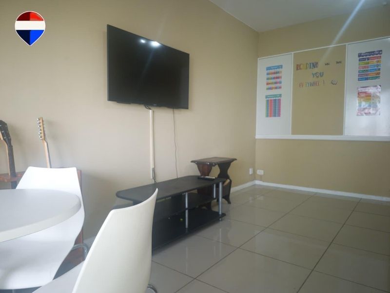 A living area featuring neutral wall tones and tiled flooring, equipped with a wall-mounted television.