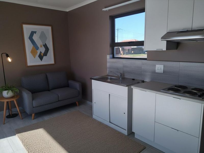 Compact open-plan living area featuring a modern kitchenette with built-in cabinetry, electric hob, extractor fan, and stainless steel sink.