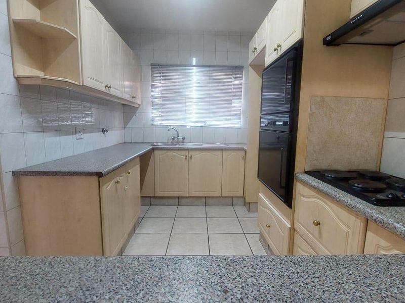 A functional kitchen featuring laminate cabinetry, granite-look countertops, built-in oven, electric hob, and tiled finishes throughout.