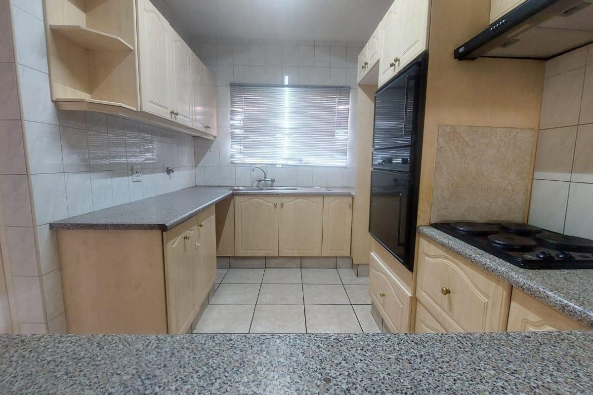 A functional kitchen featuring laminate cabinetry, granite-look countertops, built-in oven, electric hob, and tiled finishes throughout.