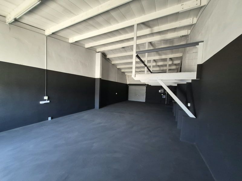 Spacious industrial utility area featuring high exposed timber ceilings, a mezzanine level, concrete flooring, and a secure roller shutter door access.